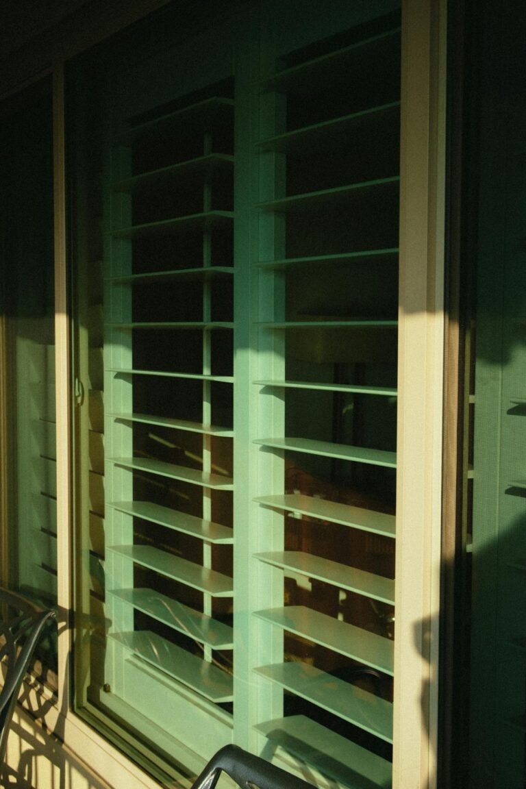 Close-up of a sunlit jalousie window with geometric patterns and green hues.